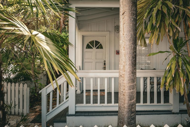 Charming tropical front porch with palm trees and white wooden railing, evoking a summer vibe